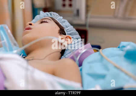 Vista lateral del niño acostado en la cama de un hospital después de la cirugía para dormir