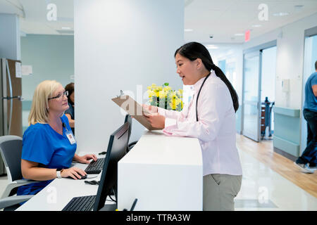 Doctora mirando portapapeles mientras habla con la enfermera en el hospital de recepción Foto de stock