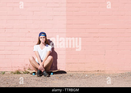 Retrato de una adolescente que sopla chicle mientras está sentado sobre skateboard contra la pared Foto de stock