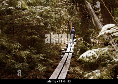 Mujer caminando sobre el viejo puente peatonal en medio de los árboles en el bosque