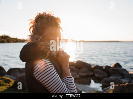Vista lateral de la mujer con los ojos cerrados en Lakeshore permanente contra el cielo despejado durante la puesta de sol