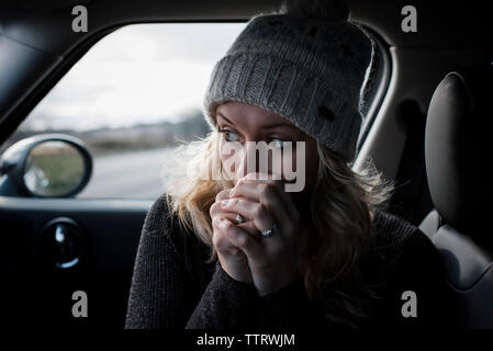 Close-up de mujer con las manos entrelazadas mirando a otro lado mientras está sentado en el coche Foto de stock