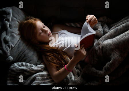 Niña leyendo un libro en la cama. Habitación oscura con luz de noche  proyección de estrellas en el techo de la sala. Guardería infantil y ropa  de cama Fotografía de stock 