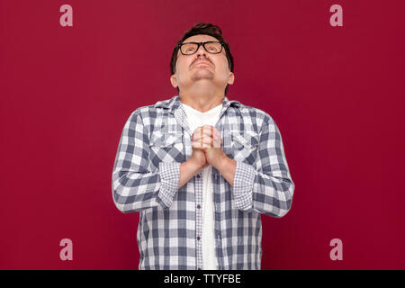 Oh Dios, por favor ayúdame. Retrato de esperanza triste preocuparse un varón de mediana edad en casual camisa a cuadros y gafas de pie, orando y mirando hacia arriba. ind Foto de stock