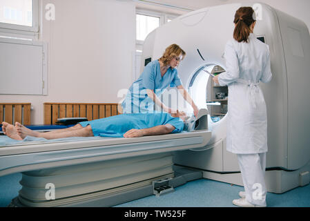 Radiólogo en bata blanca de pie cerca de escáner CT mientras prepara la enfermera paciente para diagnóstico. Foto de stock
