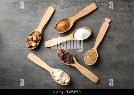 Diversos tipos de azúcar en cucharas de madera en tabla gris Foto de stock