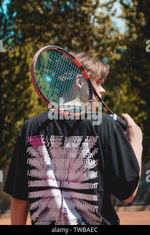 El deporte del tenis. Hombre jugando al tenis al aire libre. Retrato de  joven atractivo en camiseta blanca con la raqueta y la bola en el fondo del  cielo. Un estilo de