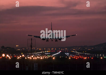 Los aviones de pasajeros de aterrizar en el Aeropuerto Internacional de Ciudad del Cabo al anochecer con la pista de aterrizaje claramente iluminado.
