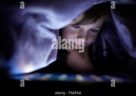 Niñito Jugando secretamente con su tableta digital, oculto bajo una manta