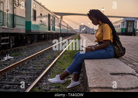 Mujer joven sentada en el andén en la estación de tren utilizando el portátil