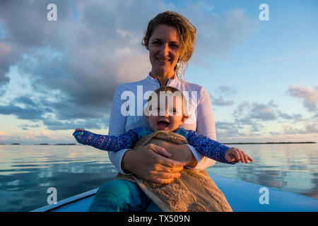 La Polinesia Francesa, Tuamotus, Tikehau, madre sosteniendo a su bebé feliz en un barco en el mar