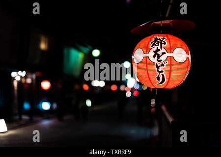 Kyoto, Japón - Abril 16, 2019: el estrecho callejón Street en el distrito Gion en primer plano de noche con faroles de papel iluminados en rojo y negro del fondo bokeh Foto de stock