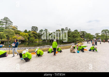 Kyoto, Japón - Abril 17, 2019: la gente trabajadores voluntarios separando la grava blanca y negra por green spring garden en el Palacio Imperial con el lago pond Foto de stock