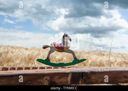 Antique, caballito está de pie sobre una valla de madera con vistas a un campo de grano