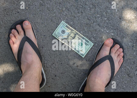 El dinero se encuentra en el pavimento bajo los pies de un joven en flip-flops Foto de stock