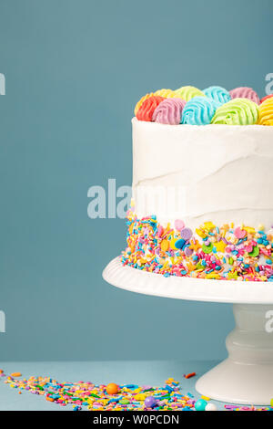 Un pastel de cumpleaños con hielo blanco y rociadas arco iris se sienta  sobre una mesa de madera sobre un fondo azul Fotografía de stock - Alamy