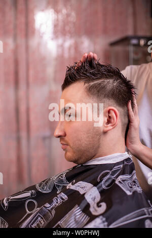 El maestro corta el cabello y la barba de los hombres en la barbería, el  peluquero hace el peinado para un hombre joven