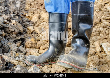 Botas de goma para de trabajo. obrero stands con sus botas de goma negra un montón de tierra Fotografía de stock -