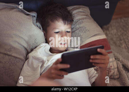 Chico jugando en tableta digital por la noche en la oscuridad del dormitorio