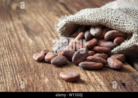 Cacao en grano de cilicio bolsa sobre un fondo de madera. Foto de stock