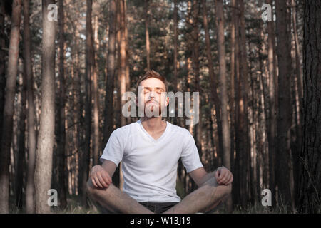 Macho joven persona meditando en el bosque. El hombre moderno se encuentra en el bosque de pinos con los ojos cerrados y disfruta del silencio de la naturaleza