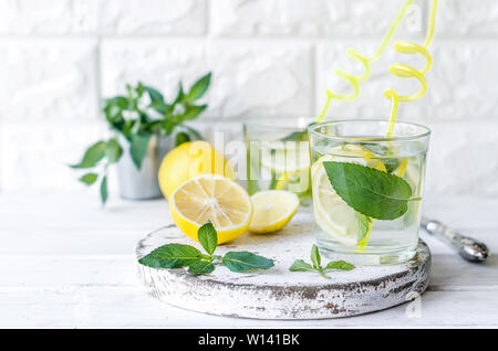Mojito cóctel en vidrio, limones y hojas de menta en bascet sobre mesa de madera blanca, cóctel de verano concepto de bebidas Foto de stock