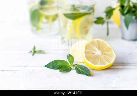 Mojito cóctel en vidrio, limones y hojas de menta en bascet sobre mesa de madera blanca, cóctel de verano concepto de bebidas Foto de stock