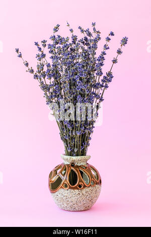 Fragante ramo de lavanda seca con pequeñas flores moradas en un hermoso jarrón de cerámica sobre un fondo de color rosa pastel. Aromaterapia y comodidad. Vi delantero Foto de stock