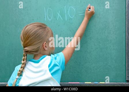 Joven chica caucásica escrito problema matemático en pizarra verde Foto de stock