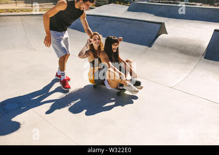 Un grupo de amigos, divertirse en el parque de skate. Joven y dos niñas jugando con un monopatín en el skate park.