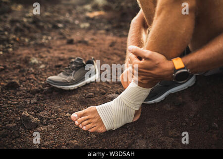 Hombre vendarse el tobillo lesionado. Las lesiones de la pierna mientras ejecutan afuera. Primeros auxilios para esguince de ligamento o tendón. Close-up sobre fondo oscuro. Foto de stock