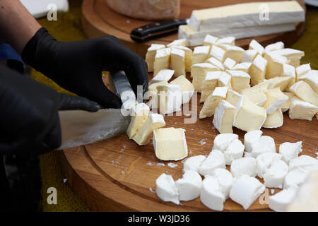 Chef-cocinero queso en lonchas sobre una tabla para cortar. Cortar los ingredientes closeup Foto de stock