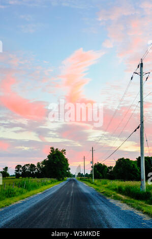 Camino de ripio en la zona rural de madera con postes eléctricos bajo rojo atardecer nubes. Foto de stock
