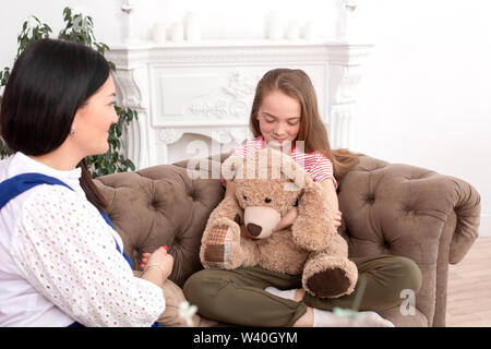 Madre e hija pasan tiempo juntos, sentarse en el sofá y chat. Ocio madres e hijas. Niña triste abrazos Teddy Vedmed y llora cerca de mamá. Foto de stock