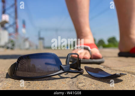 Gafas negras yacen en la carretera cerca del muchacho en sandalias Foto de stock
