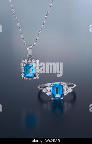 Un colgante de oro blanco y el anillo con topacio azul talla esmeralda rodeado de piedras preciosas y diamantes de acento. Foto de stock