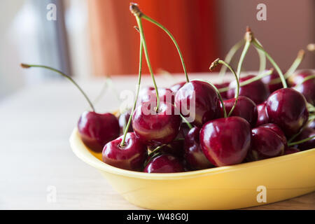 Jugosas y maduras bayas de un rojo cereza dulce en un recipiente amarillo sobre la mesa por la ventana