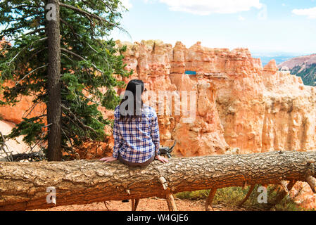 Viajero mujer sentada sobre el tronco de un árbol caído disfrutando la vista en Bryce Canyon, Utah, EE.UU.