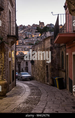Vista desde un callejón en Ragusa Ibla a Ragusa Superiore al anochecer, Ragusa, Sicilia, Italia Foto de stock