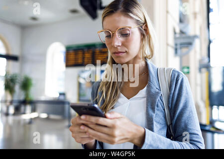 Mujer joven texto con su teléfono móvil en la estación de tren hall Foto de stock