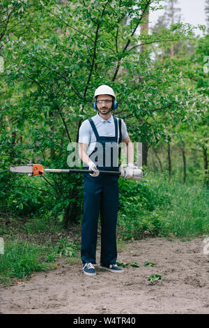 Jardinero serio en casco podar los árboles con pértiga telescópica vio y  mirando a la cámara Fotografía de stock - Alamy