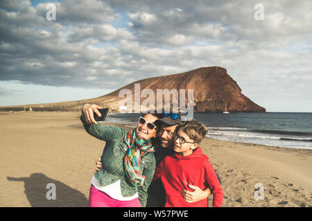 Mamá papá con hijo teniendo selfie sonriente y feliz en la playa, cerca del océano. Los padres con niños en vacaciones haciendo fotos para recuerdos de un exótico