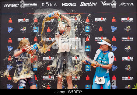 Hamburgo, Alemania. 28 de julio de 2019. Triatlón Ironman: World Series/Campeonato Alemán, mujeres: Sarah Piampiano (l-r) de EE.UU. (2º lugar), Susie Cheetham desde Gran Bretaña (1º lugar) y Julia Gajer desde Süßen (Alemania, 3er lugar y mejor alemán) están en el podio y beber cerveza. Crédito: Georg Wendt/dpa/Alamy Live News Crédito: dpa picture alliance/Alamy Live News Foto de stock