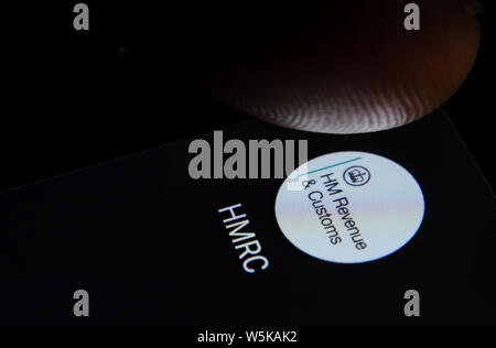 El HMRC app icono en la pantalla del smartphone con píxeles visibles y el dedo a punto de iniciarlo. Foto de stock
