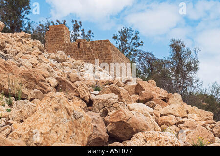 Bajo el ángulo de la época mameluca de piedra de molino de harina en Ein Gedi primavera en Israel con una ladera rocosa en el primer plano y el cielo nublado en el fondo Foto de stock