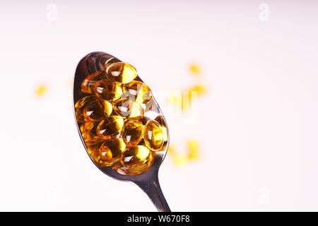 Las cápsulas con vitamina en una cucharadita sobre un fondo blanco. Foto de stock