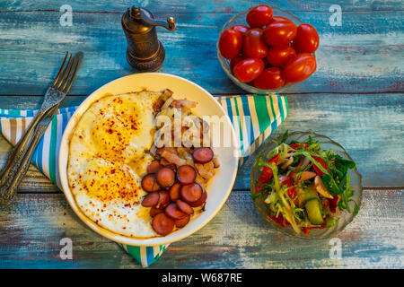 Huevos revueltos con bacon, cebolla y salchicha. En un plato sobre la mesa. Foto de stock
