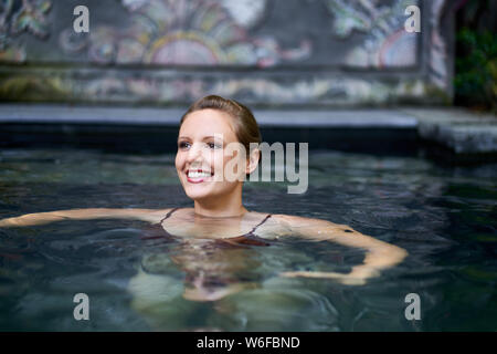Mujer sonriente joven nadar al aire libre en la piscina spa exótico del lujoso hotel durante unas vacaciones tropicales en Bali Foto de stock