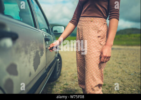 Una joven mujer es desbloquear su automóvil en la naturaleza en un día de verano