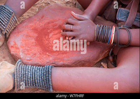 Mujer Himba aplasta arcilla roja, entonces esto se utiliza para recubrir su cabello. Fotografiado en una aldea Himba, Epupa Falls, Kaokoland, Namibia, África Foto de stock